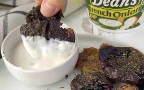 Smashed, baked purple yam dipping into Dean's French Onion Dip in a ceramic bowl